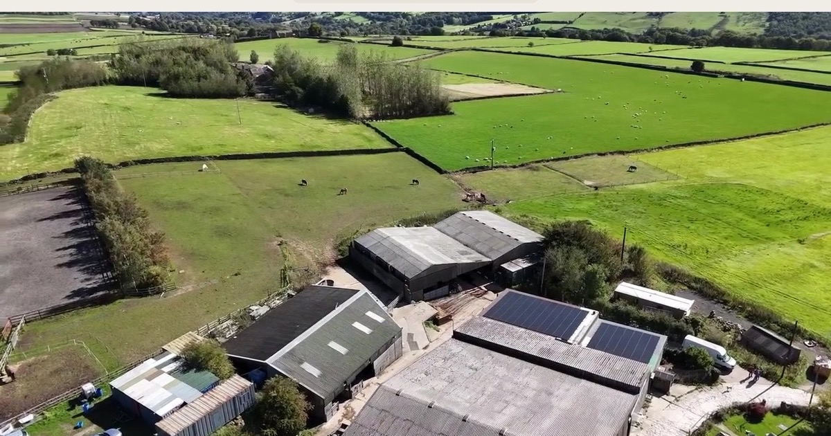 Two glass-walled padel courts on a farm on the edge of the Peak District, with a timber barn and open fields behind them